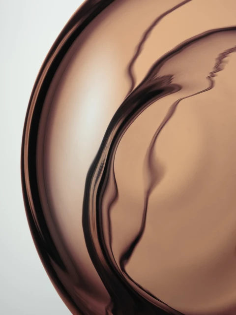 Abstract studio shot of reflective copper metal surface showcasing curved lines, and unique light play in an artistic composition.