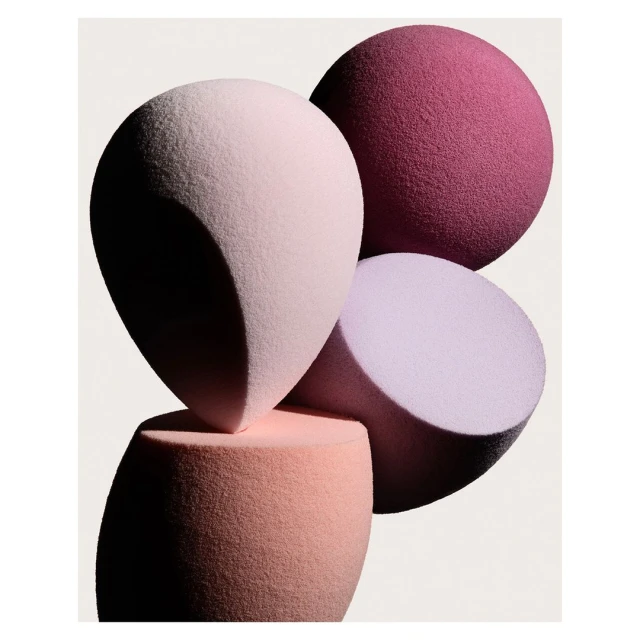 Close-up of stacked makeup sponges in pink, lavender, and burgundy tones against a bright white background, beauty product.