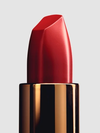 Close-up macro shot of a vibrant red lipstick bullet in a reflective gold case against a neutral grey background