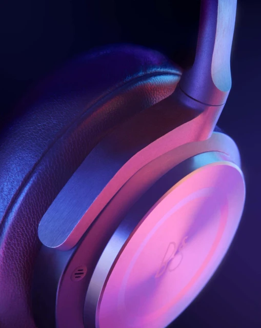 Close-up of wireless over-ear headphones with a metal construction and leather earcups, illuminated with a pink and blue gradient light.