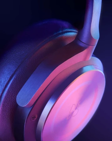 Close-up of wireless over-ear headphones with a metal construction and leather earcups, illuminated with a pink and blue gradient light.
