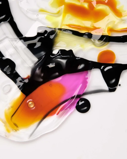 Abstract close-up shot of translucent gels and colorful liquids blending together, creating textures and patterns on a white surface.