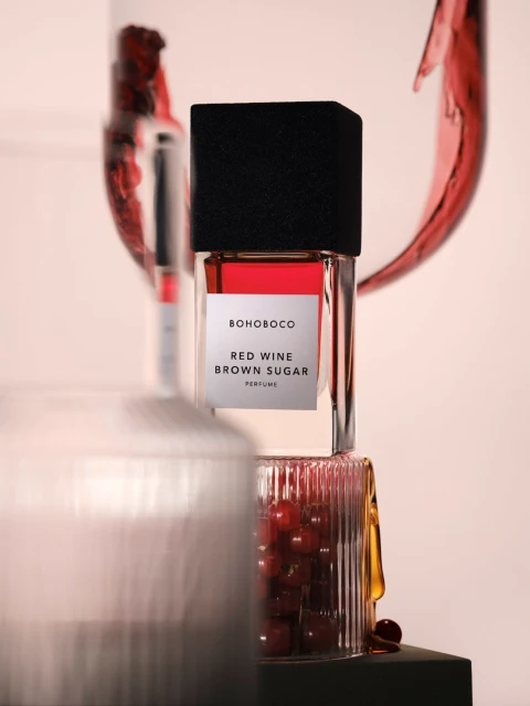 Bohoboco Red Wine Brown Sugar perfume bottle, featuring geometric shapes and red liquid with a pink background in a studio setting.