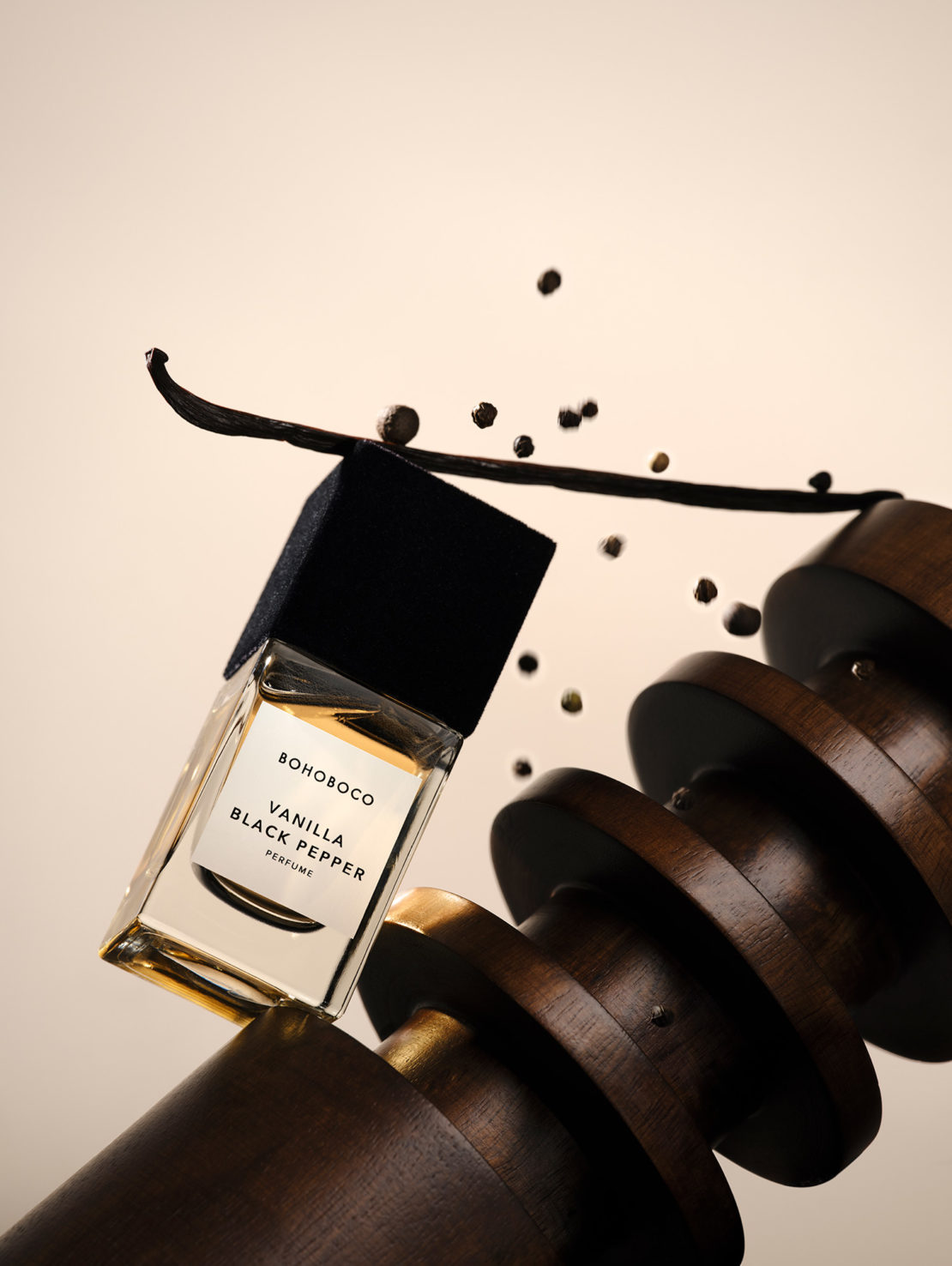 BOHOBOCO Vanilla Black Pepper perfume bottle with vanilla bean and black peppercorns, balanced on wood circles, studio shot.