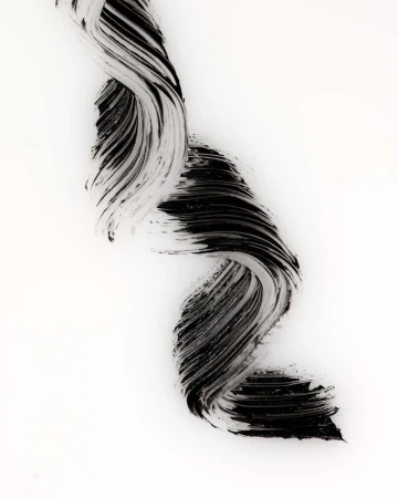 Textural abstract image of a swooping wave-like pattern of black mascara against a stark white backdrop, beauty product advertisement.