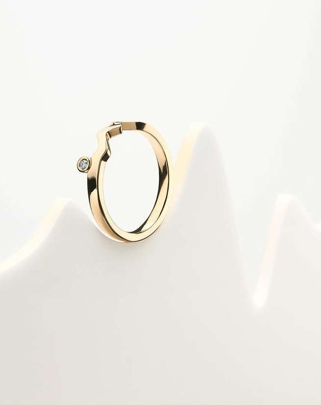 Close-up of a gold ring with a diamond accent, resting on a white surface with soft lighting and elegant presentation. 