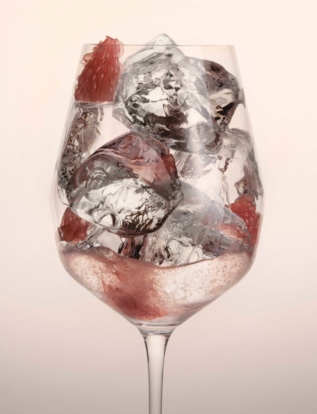 Wine glass filled with large ice cubes and a pink drink with pieces of grapefruit; refreshing beverage presentation.