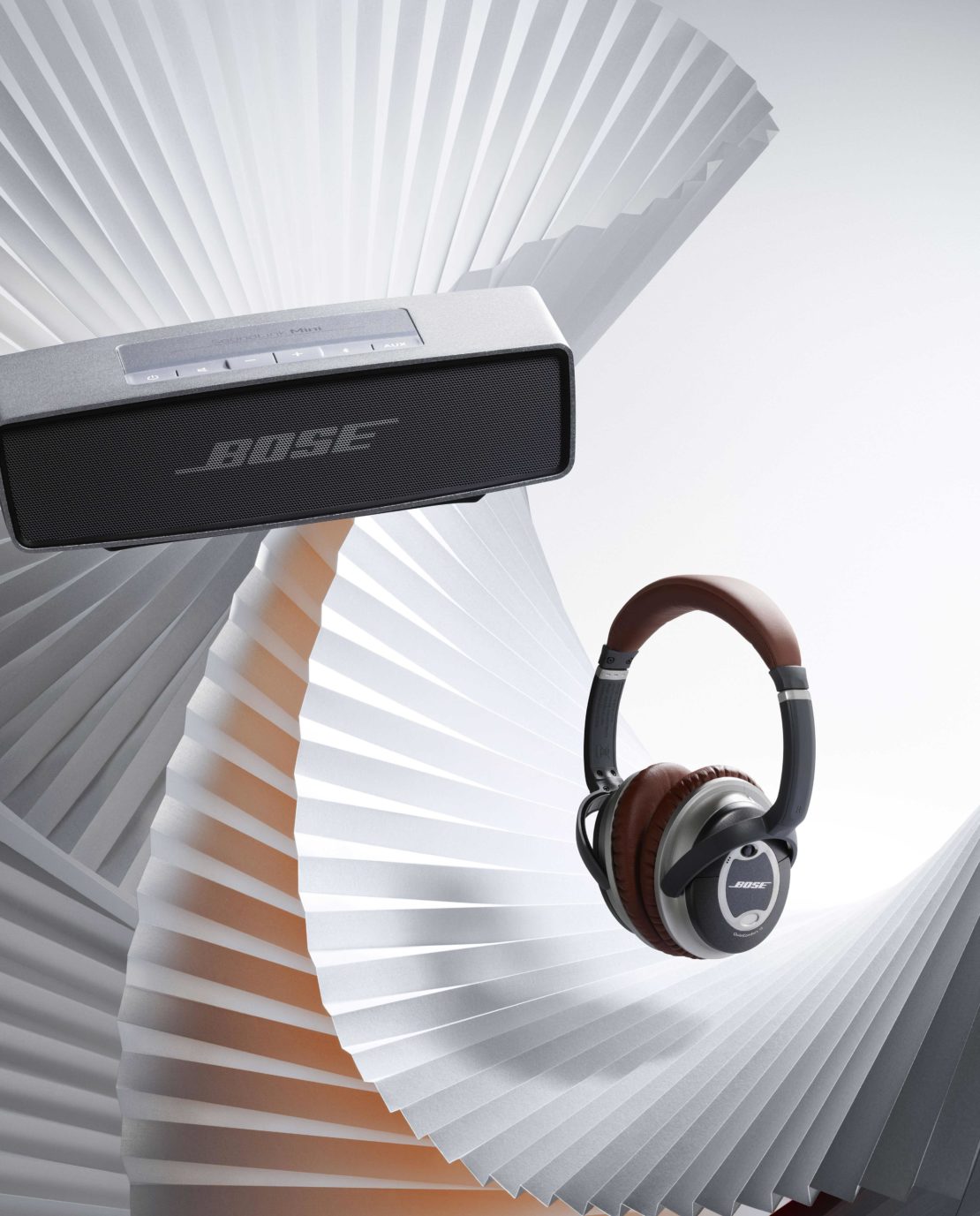 Bose SoundLink speaker and QuietComfort headphones with a grey paper fan background, product photography, studio shot.