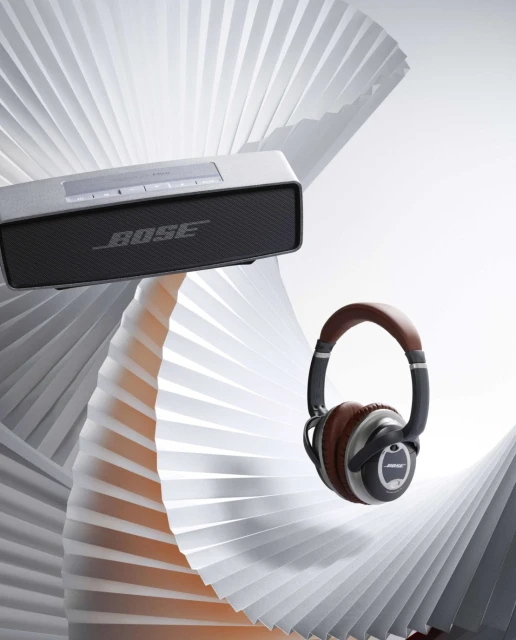 Bose SoundLink speaker and QuietComfort headphones with a grey paper fan background, product photography, studio shot.