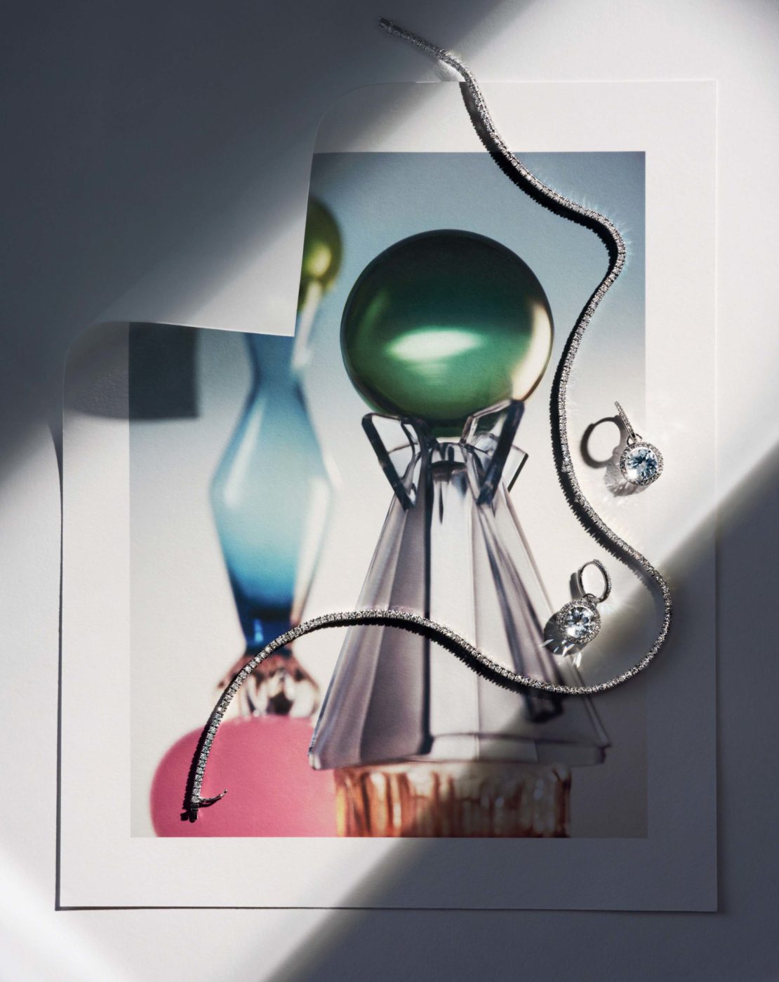 Still life of jewelry, including a silver necklace and earrings with blue stones, displayed on a print of colorful glass art.