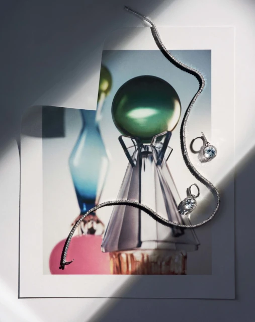 Still life of jewelry, including a silver necklace and earrings with blue stones, displayed on a print of colorful glass art.
