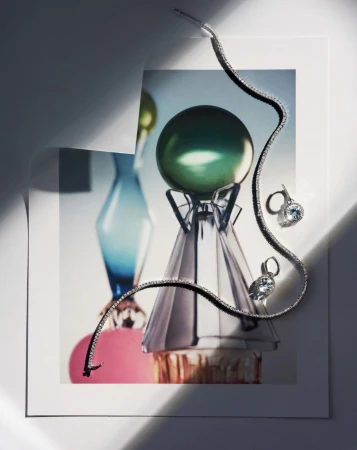 Still life of jewelry, including a silver necklace and earrings with blue stones, displayed on a print of colorful glass art.