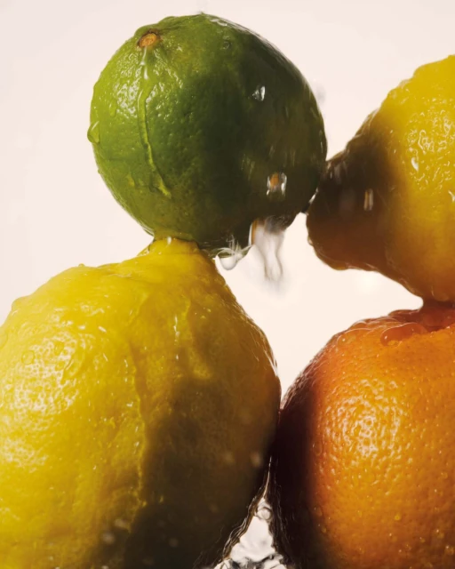 Studio shot of lime, lemons, and orange stacked, glistening with water droplets against a clean background, showcasing fresh citrus fruits.