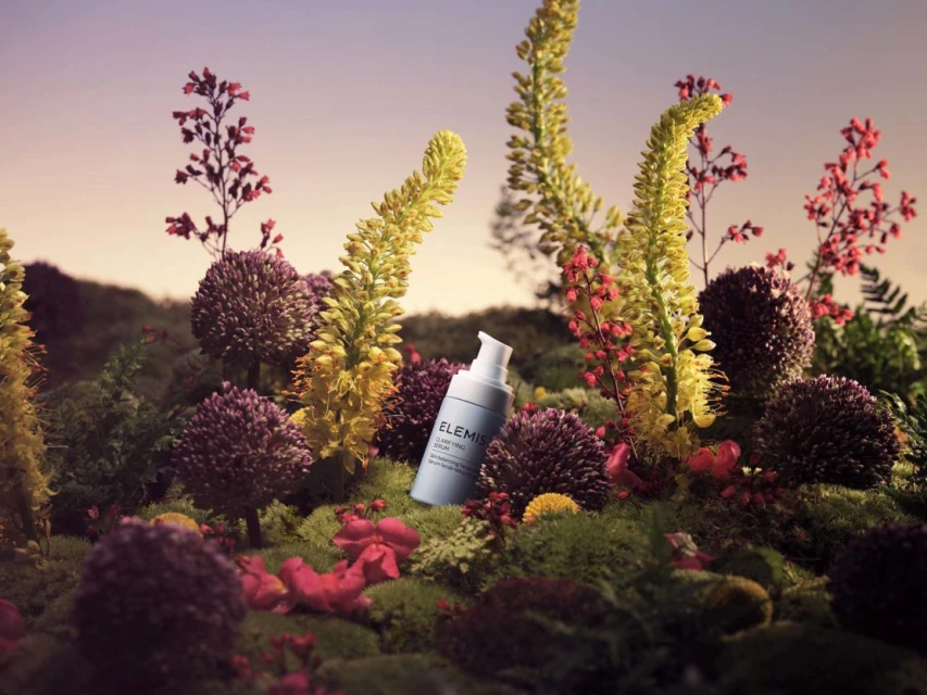 Still life of light blue ELEMIS skincare bottle among colorful wildflowers and mossy ground cover against a soft, light gradient sky.