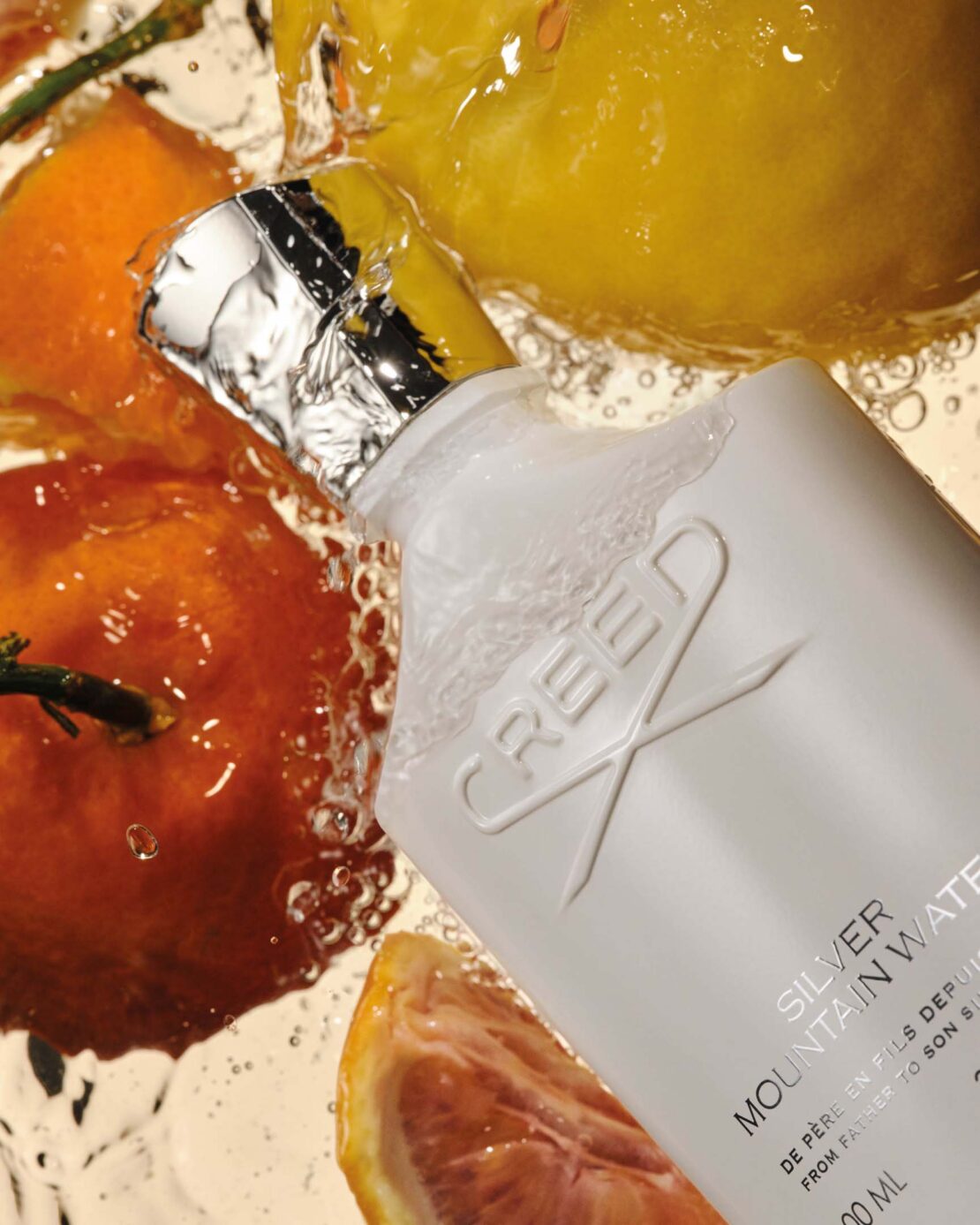 Creed Silver Mountain Water perfume bottle with sliced oranges and lemons surrounded by bubbles against a light-toned background.