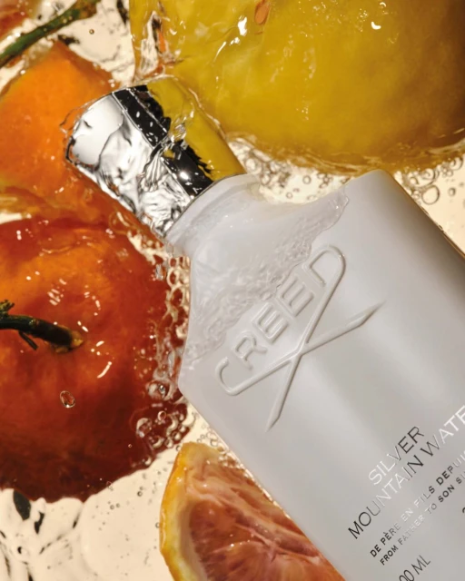 Creed Silver Mountain Water fragrance bottle surrounded by water droplets and citrus fruits in a bright studio product shot.