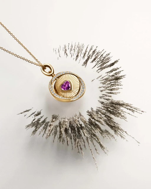 Elegant gold necklace pendant with purple heart-shaped gemstone surrounded by diamonds displayed with a ring of dark powder.