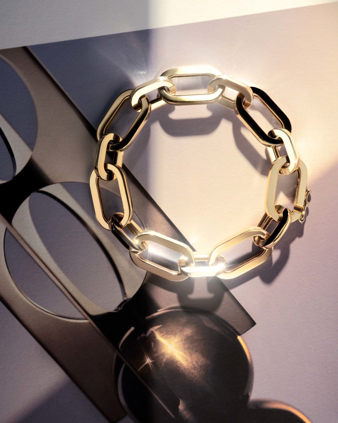 Close-up studio shot of a gold chain-link bracelet with warm, diffused lighting and a modern grey and white background.