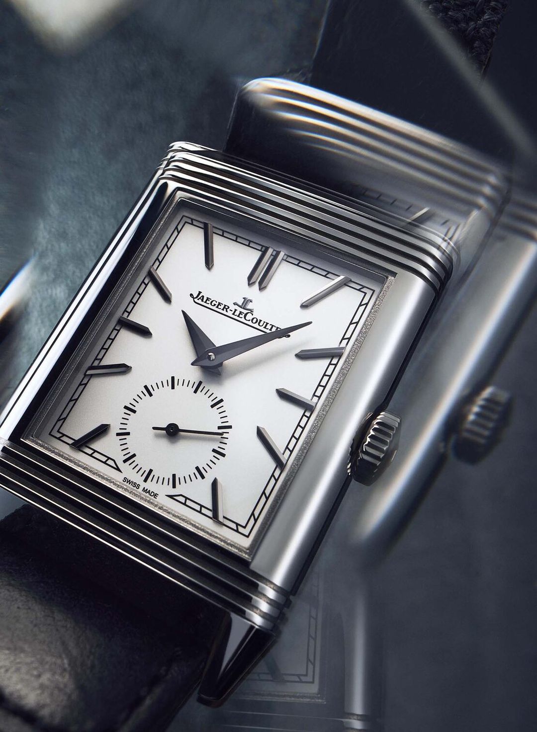 Close-up studio shot of a Jaeger-LeCoultre watch with a silver case, black leather strap, and white face displaying time.