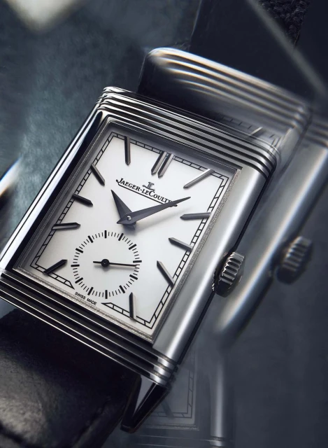Close-up studio shot of a Jaeger-LeCoultre watch with a silver case, black leather strap, and white face displaying time.