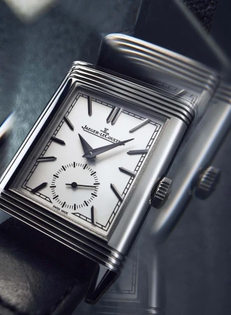 Close-up studio shot of a Jaeger-LeCoultre watch with a silver case, black leather strap, and white face displaying time.