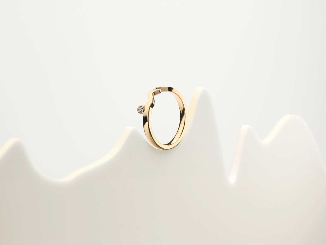Close-up of a single gold hoop earring with a diamond accent on a white display, showcasing minimalist jewelry design.