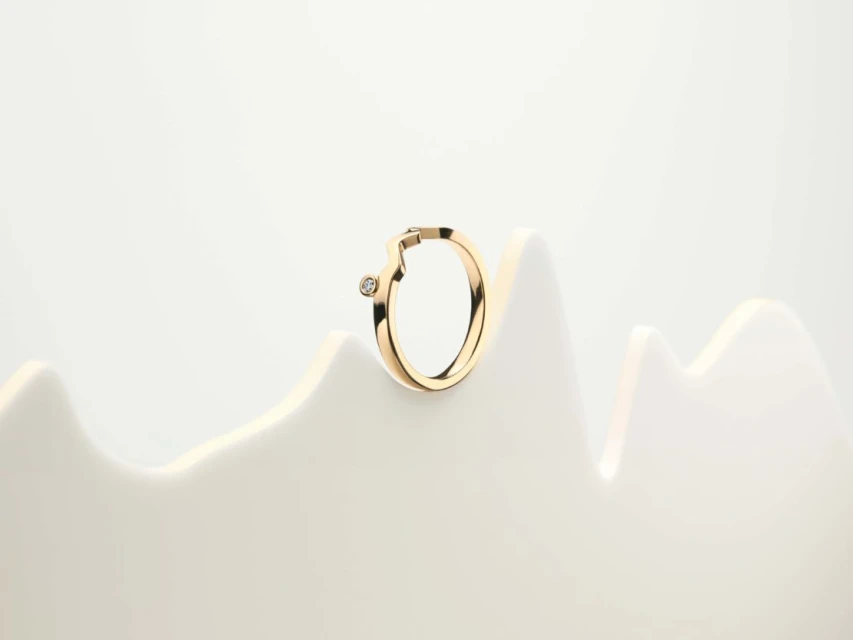 Close-up of a single gold hoop earring with a diamond accent on a white display, showcasing minimalist jewelry design.