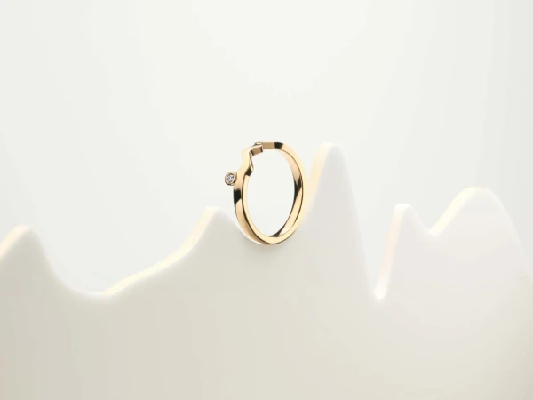 Close-up of a single gold hoop earring with a diamond accent on a white display, showcasing minimalist jewelry design.