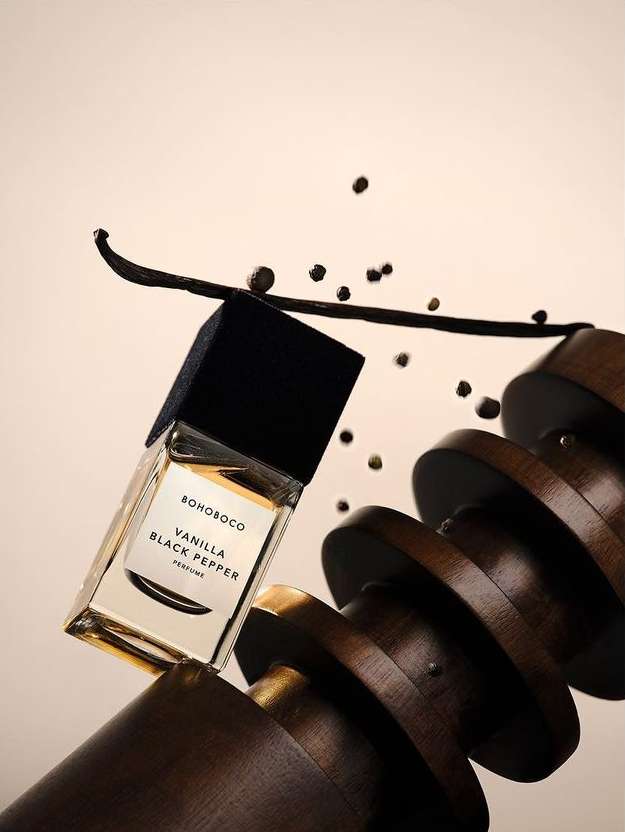 Fragrance bottle with vanilla bean and black peppercorns in a studio setting, featuring a modern and sophisticated composition.