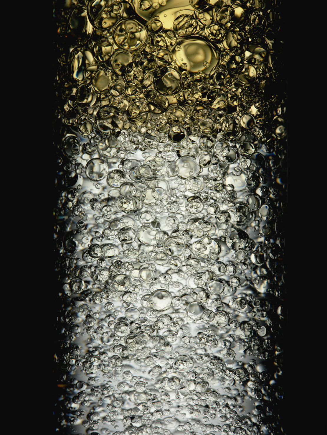 Macro photograph of transparent liquid with round bubbles, featuring golden and gray hues against a solid black background.