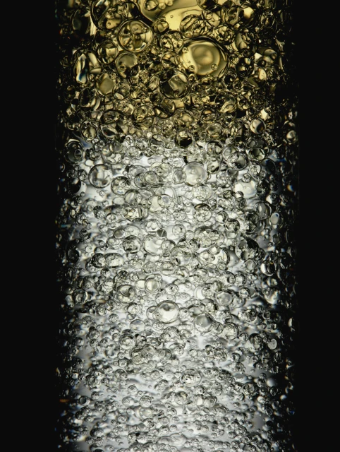 Macro photograph of transparent liquid with round bubbles, featuring golden and gray hues against a solid black background.