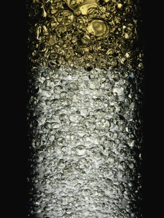 Macro photograph of transparent liquid with round bubbles, featuring golden and gray hues against a solid black background.