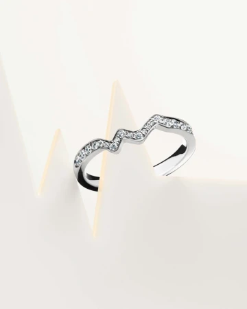 Close-up of a curved silver ring with rhinestones, displayed on a white surface with geometric paper forms, emphasizing jewelry and design.