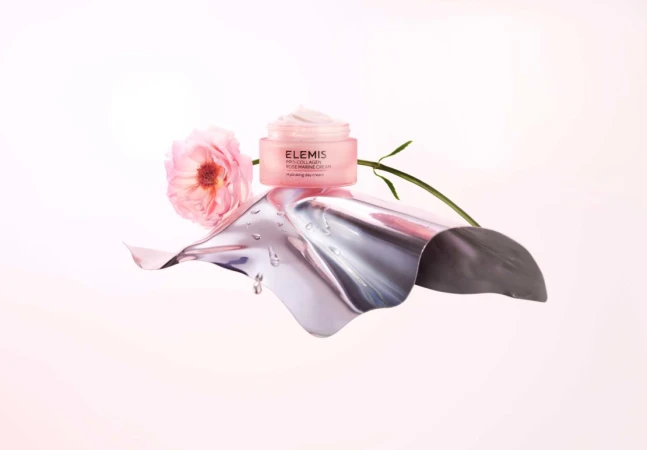 Product shot of Elemis Pro-Collagen Rose Marine Cream on a metallic surface with a pink rose against a gradient pink backdrop.