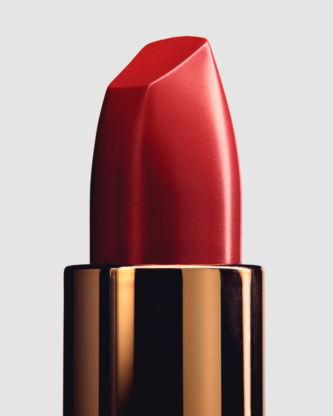 Macro shot of a vibrant red lipstick with a glossy finish, set against a neutral background. Cosmetic beauty shot with a gold container.