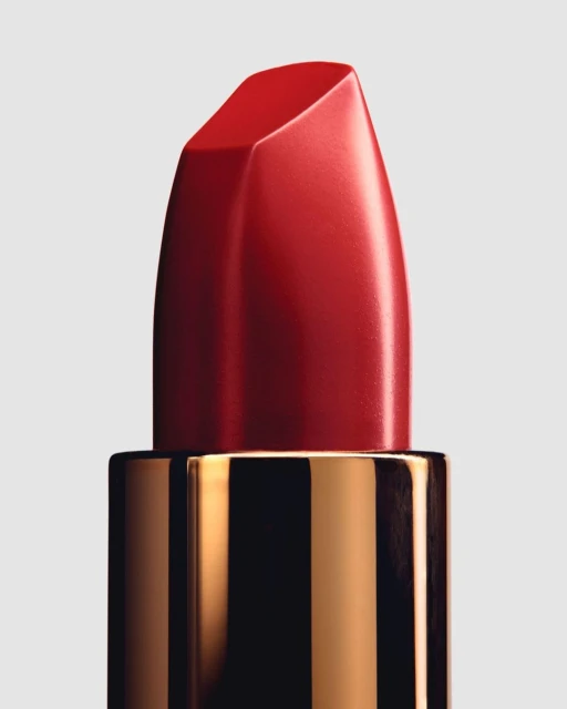 Macro shot of a vibrant red lipstick with a glossy finish, set against a neutral background. Cosmetic beauty shot with a gold container.