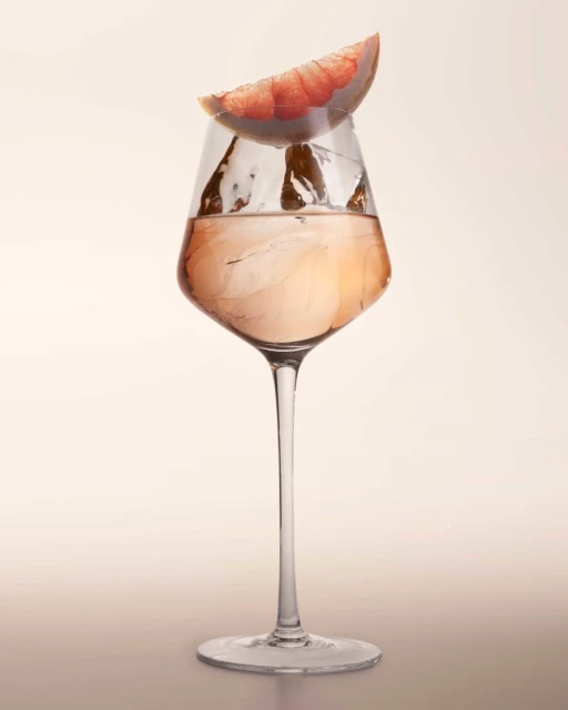 Tall glass of pink grapefruit cocktail drink with ice, isolated on light surface. Studio shot with neutral background.