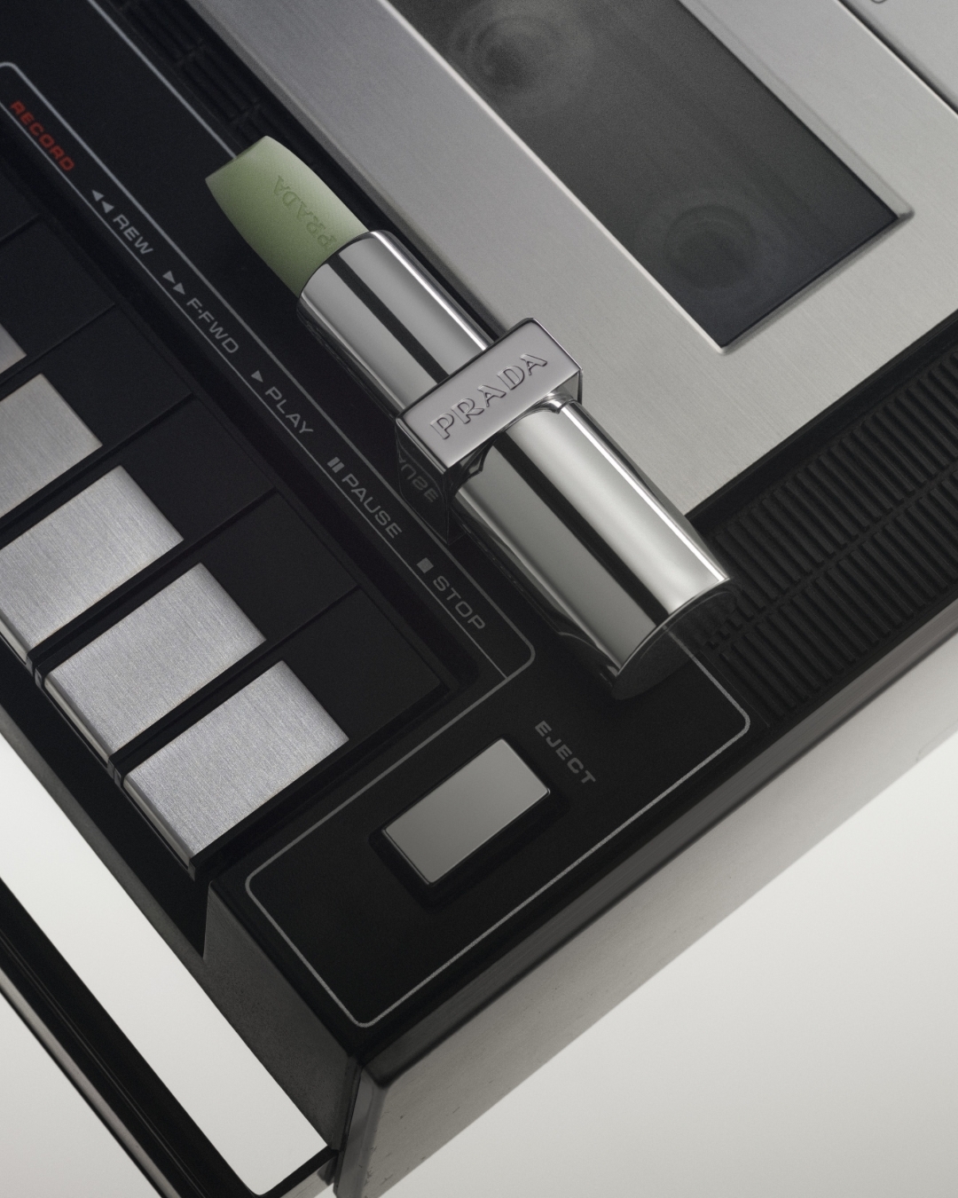 Close-up studio shot of Prada lipstick on a control panel, highlighting black, silver, and metallic textures. Product and technology meet.