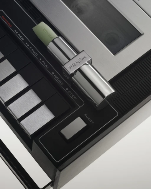 Close-up studio shot of Prada lipstick on a control panel, highlighting black, silver, and metallic textures. Product and technology meet.