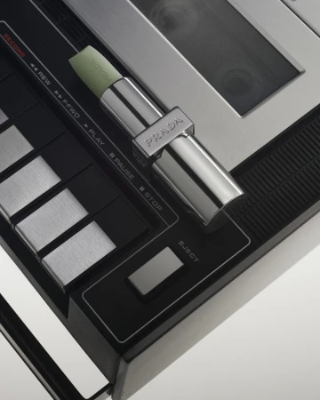 Close-up studio shot of Prada lipstick on a control panel, highlighting black, silver, and metallic textures. Product and technology meet.