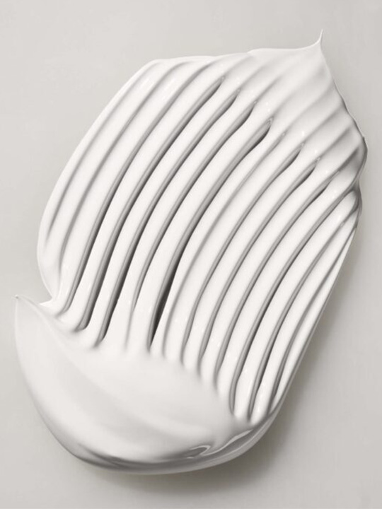 White cream swatch with parallel ridges on a light gray background, showcasing texture and smooth application for beauty or skincare.