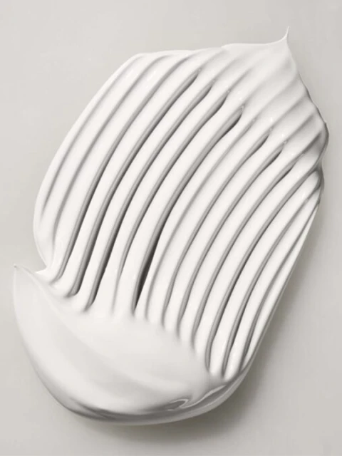 White cream swatch with parallel ridges on a light gray background, showcasing texture and smooth application for beauty or skincare.