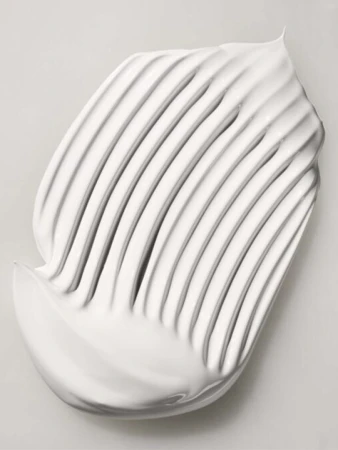 White cream swatch with parallel ridges on a light gray background, showcasing texture and smooth application for beauty or skincare.