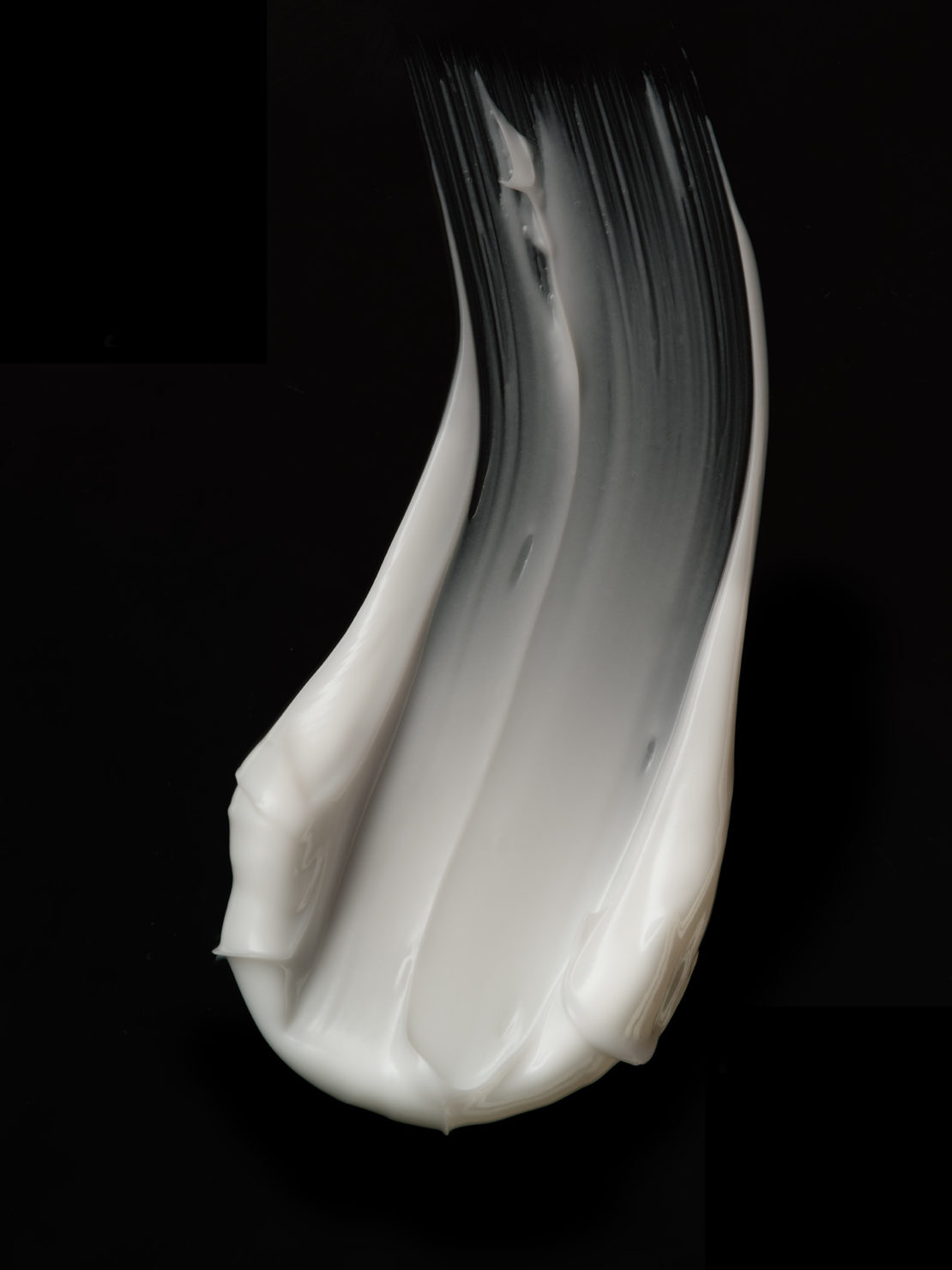 Close-up of a curved smear of white cosmetic cream against a black background, highlighting texture and skincare concept.