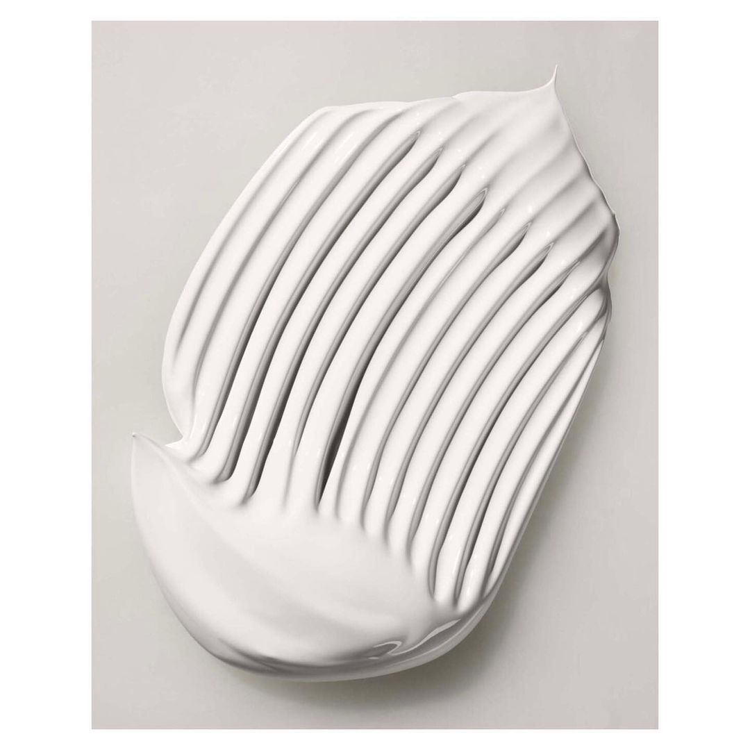 Close-up shot of a swirl of white cream product with distinct ridges, set against a light grey backdrop, highlighting the texture.