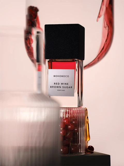 BOHOBOCO Red Wine Brown Sugar perfume bottle displayed in an artistic composition with glass containers and red liquid details.