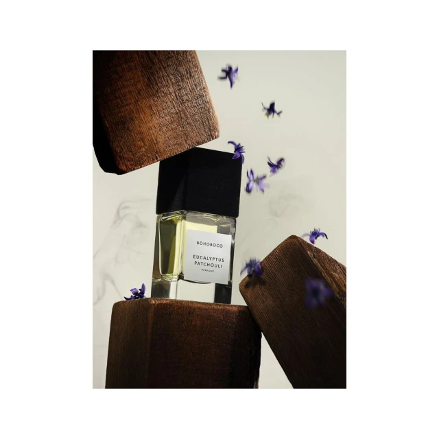 Elegant perfume bottle by Bonoboco is displayed among violet flowers and wooden blocks, capturing a natural and aromatic essence.