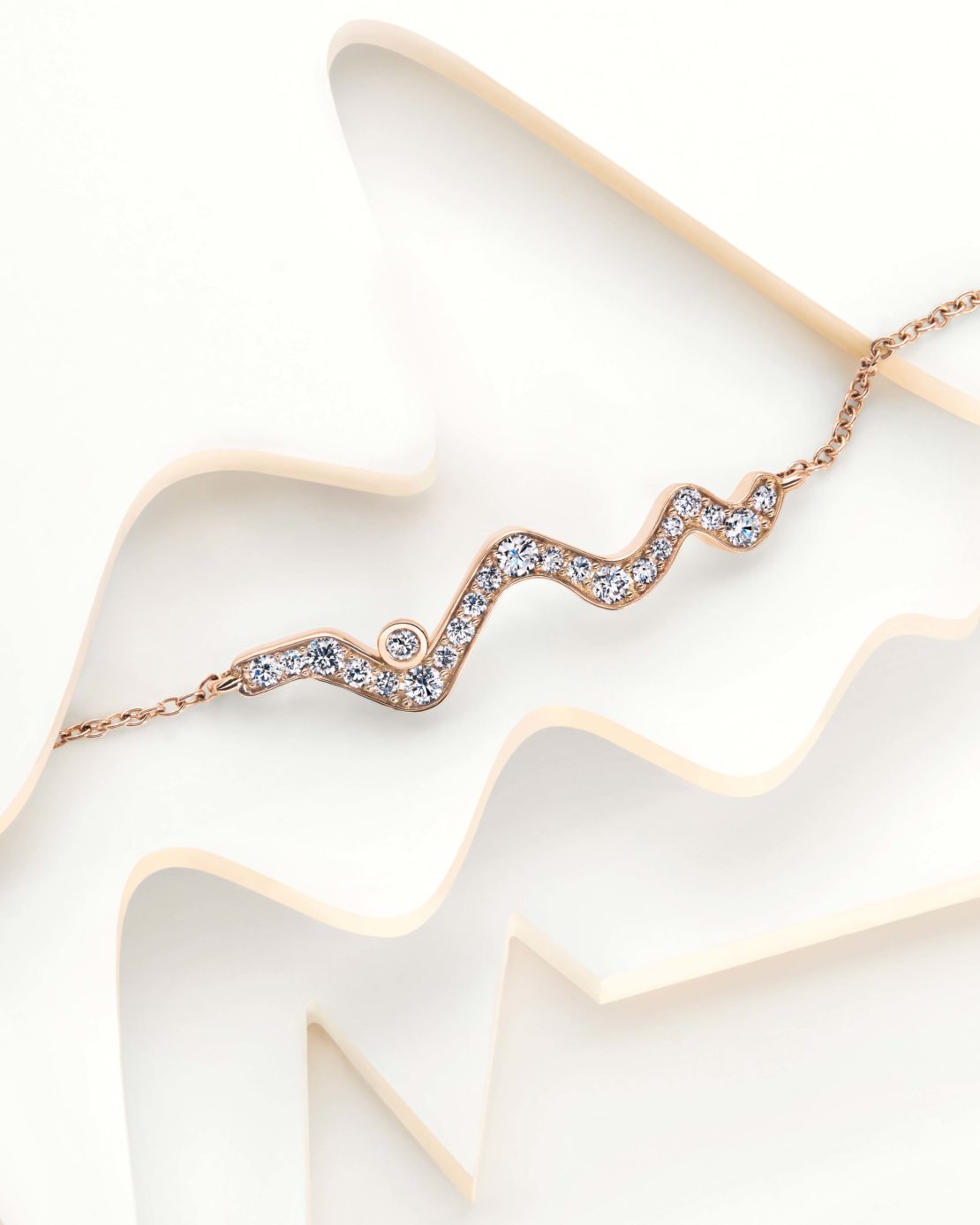 Rose gold necklace with diamonds on a white wavy surface, offering a clean and elegant jewellery presentation, ideal for fashion or beauty.
