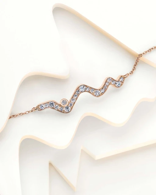 Rose gold necklace with diamonds on a white wavy surface, offering a clean and elegant jewellery presentation, ideal for fashion or beauty.
