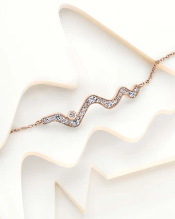 Rose gold necklace with diamonds on a white wavy surface, offering a clean and elegant jewellery presentation, ideal for fashion or beauty.